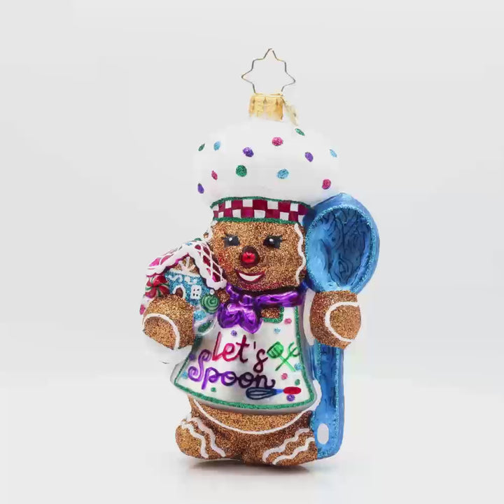Spoonful of Sweetness ornament. This gingerbread man is wearing a festive chef's outfit, spoon in hand, and gingerbread house in the other. Video.