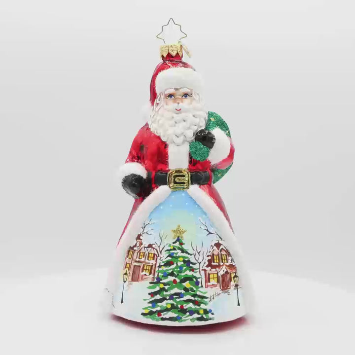 St. Nick's Winter Wonderland ornament. Santa stands amidst a picturesque snowy village. The hand-painted scene features twinkling lights and cozy homes surrounding a Christmas tree in the center. Video.
