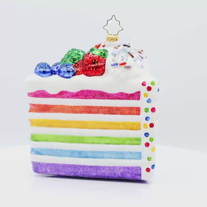 Slice of Joy ornament. A tall slice of rainbow layered cake with sprinkles and fruit on top. Video.