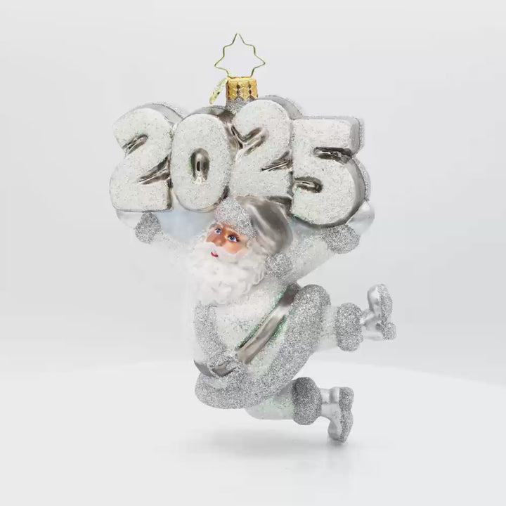Oh, Shiny Night Ornament! Santa is shining bright, ready to spread holiday cheer. Dressed in a shimmering silver suit and a sparkling hat. "2025" is held above his head in similar colors. Video.