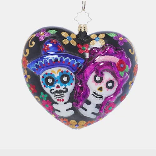 Video - Ornament Description - Sugar Skull Sweethearts: Remember those we've lost and celebrate love and life with this brightly colored heart-shaped ornament. Beautiful stylized flowers adorn one side while two sugar skull lovers wink out from the other on this Día de los Muertos-inspired ornament. This video shows the ornament spinning slowly. 