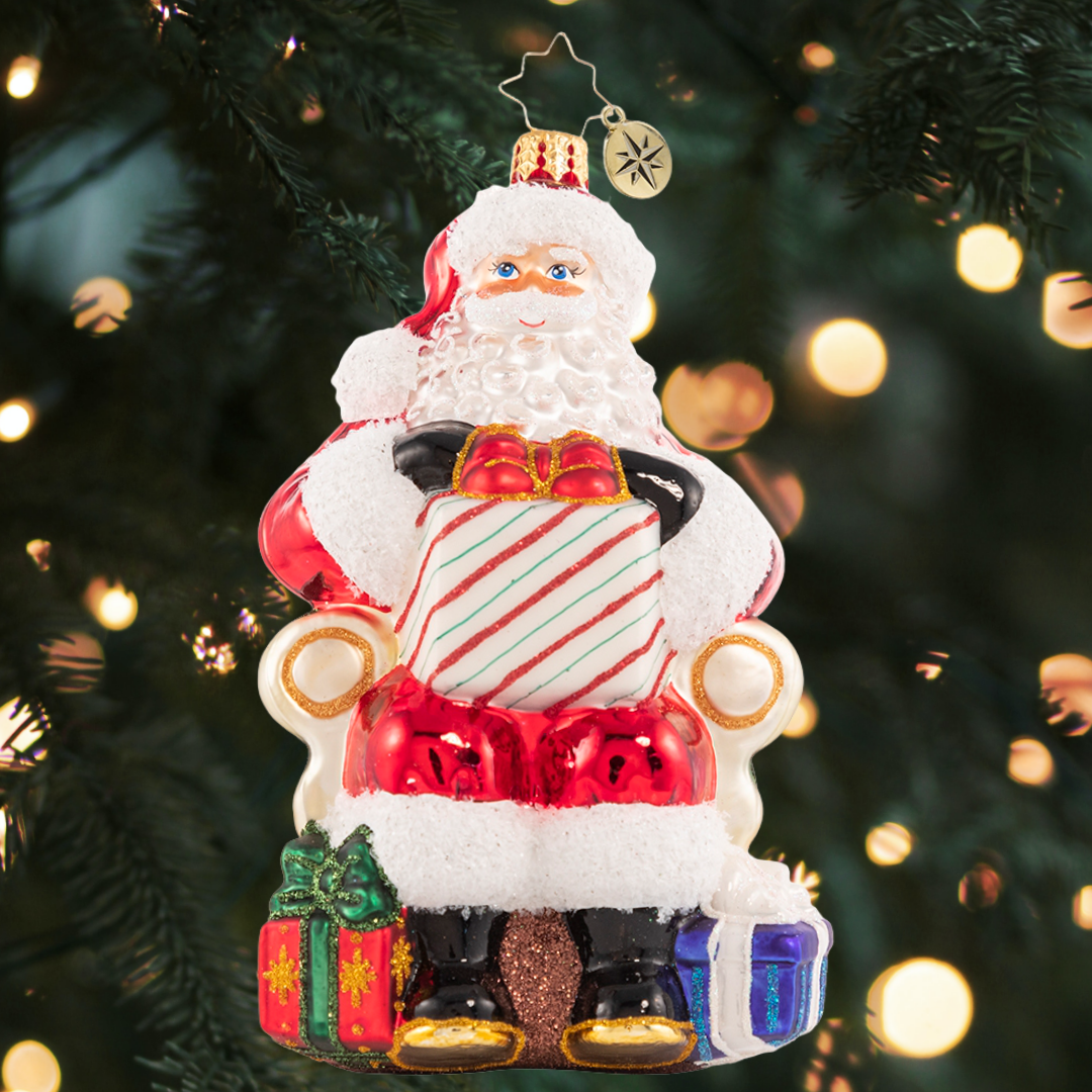 Ornament Description - Santa's Lap of Luxury: Santa relaxes on his signature velvet chair, ready to hear the wishes of countless good little boys and girls. Naughty or nice, Santa always delivers!
