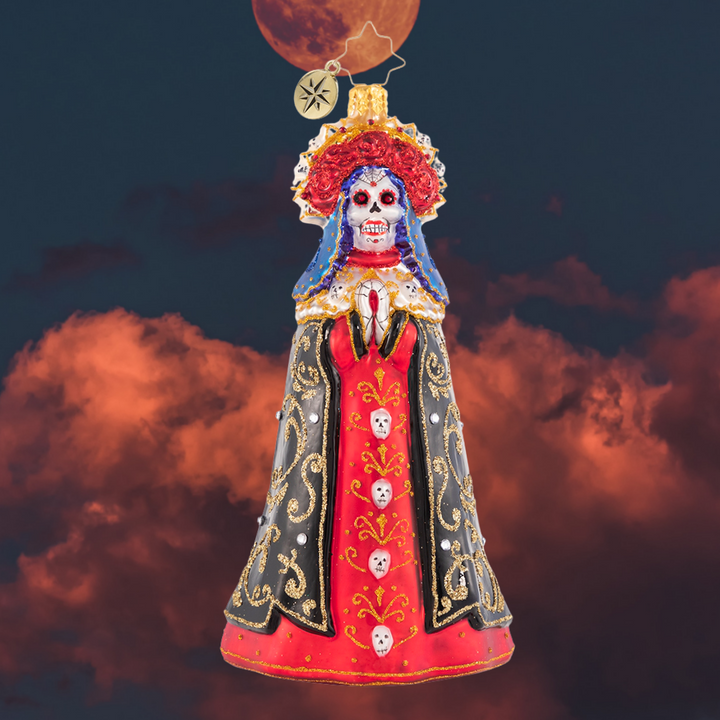 Ornament Description - Lady of Shadows: Diosa mia! Crowned with a gilded flower halo and traditional threads of gold, La Catrina arrives to pay tribute at the altar.