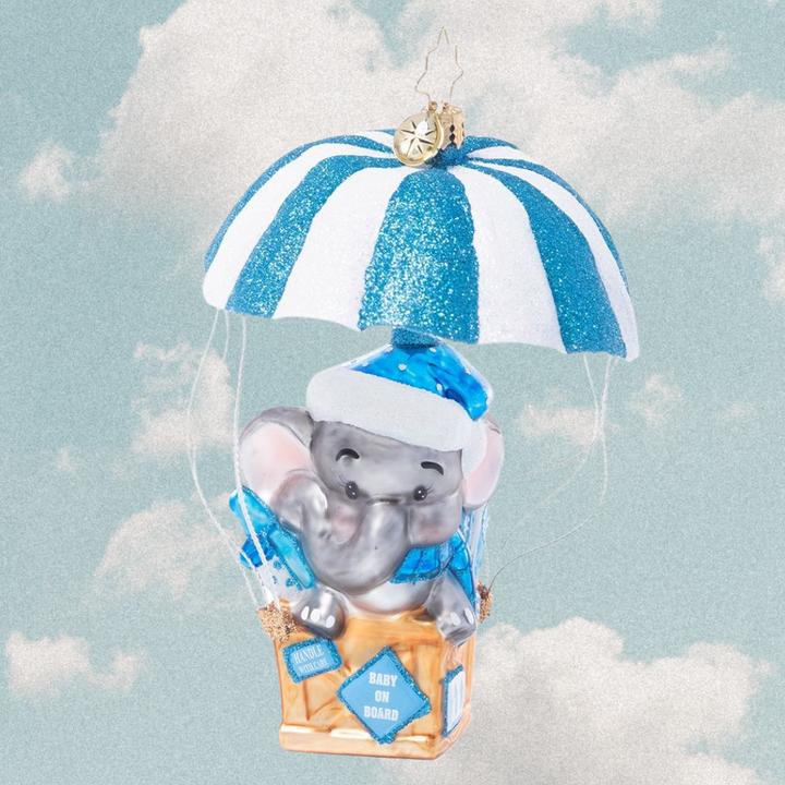 Ornament Description - Bundle of Joy Baby: Baby on board! Welcome the newest little one in your life with this adorable ornament featuring a sweet baby elephant floating in on a blue and white air mail parachute.