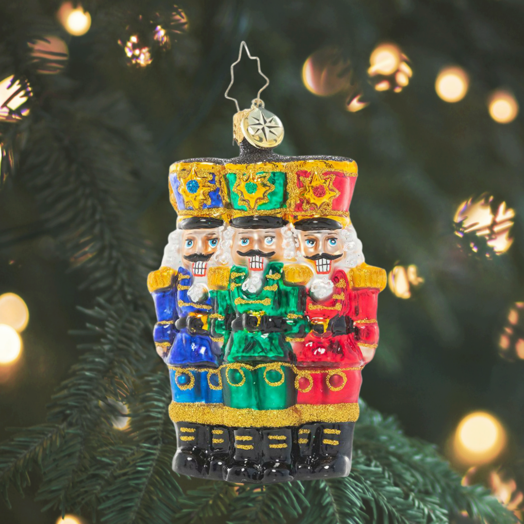 Ornament Description - The Nut-Cracking Pack Gem: Thrice as nice! A trio of nutcracker soldiers stand together, grinning in royal uniforms of bright Christmas jewel tones.