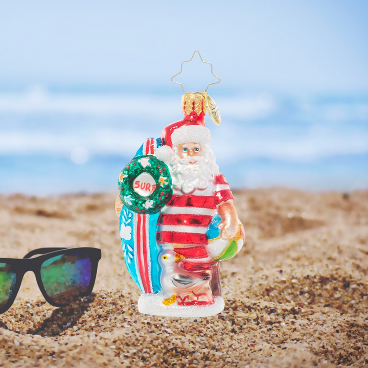 Ornament Description - Wishing For Waves Santa Gem: Ho-ho-hang ten! Santa looks ready to catch a wave as he waits for the surf report holding his bright blue surfboard.
