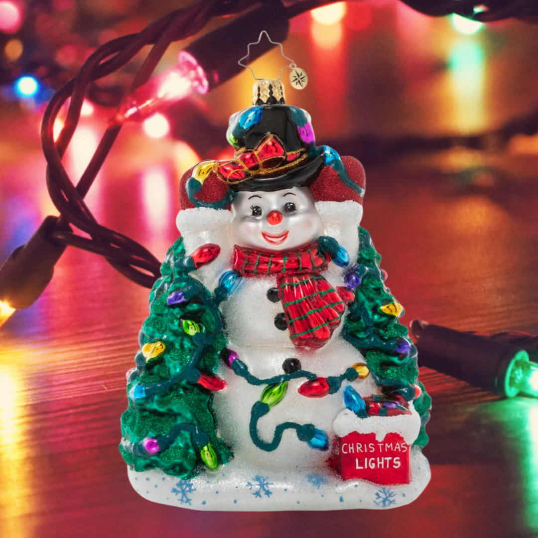 Ornament Description - Let There Be Lights: This frosty snowman has been wrestling with his Christmas lights all day long, and he's at last down to hanging his final strand. He's glad you're here to admire his holiday handiwork!