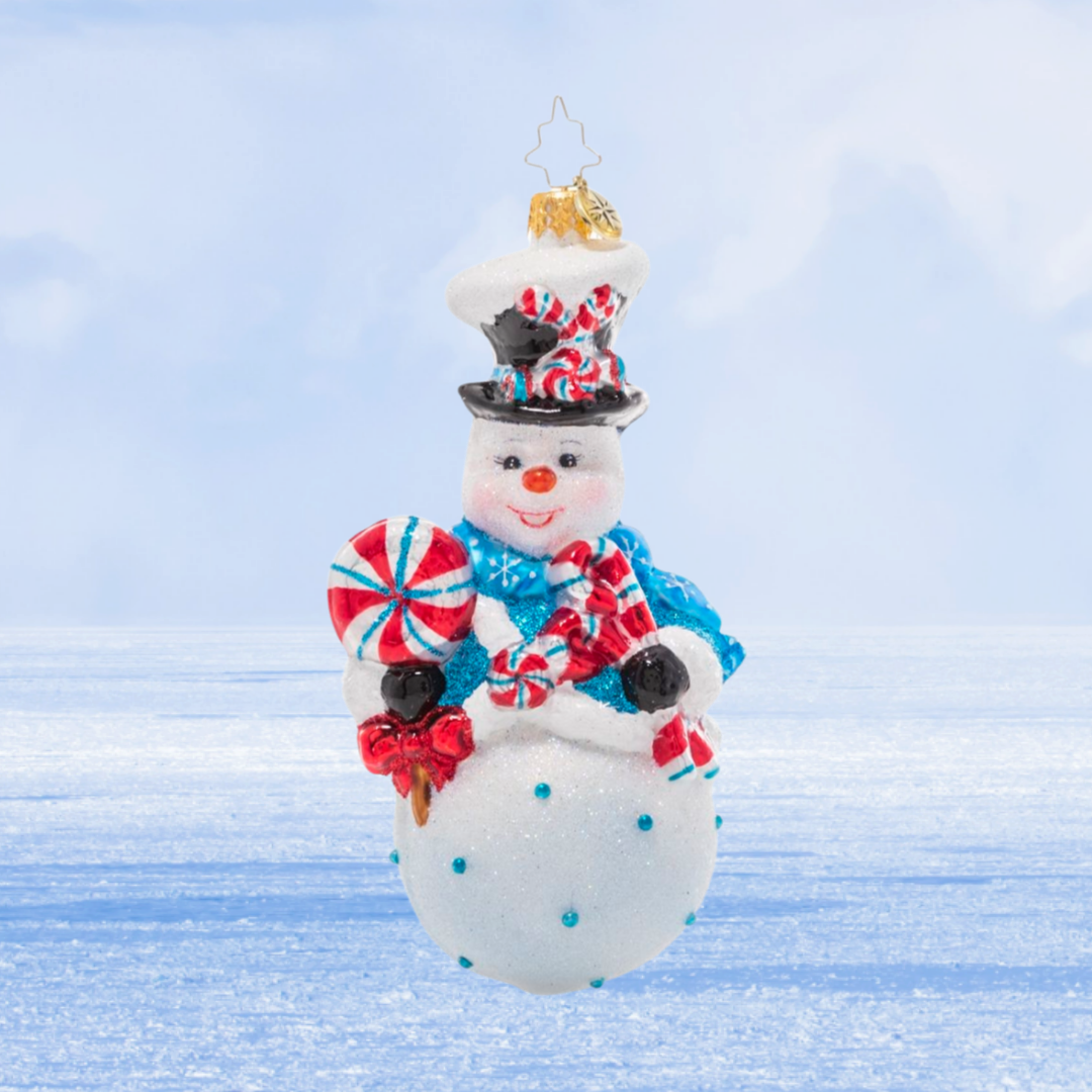 Ornament Description - Minty Magic Snowman: Make this holiday season extra sweet with this whimsical treat-toting snowman! His rosy cheeks suggest he's been playing in the snow all day, so he's ready to wind down with his favorite sweet snacks!