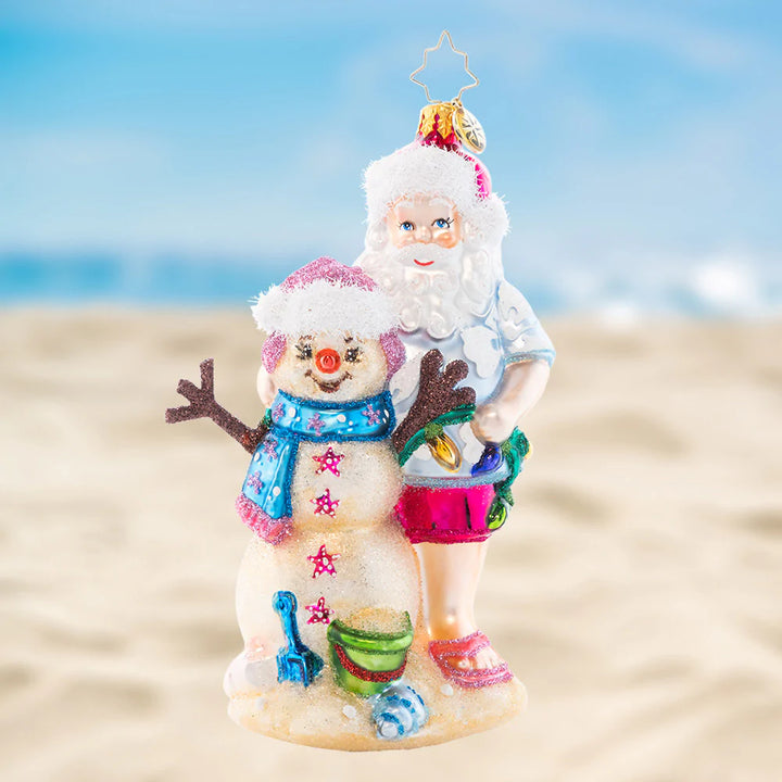 Ornament Description - Sandy Snow Team: Hang back with this Santa on the beach as the waves are in reach. Build a sandyman as best as you can, to create a cheery team with a Christmas plan. 