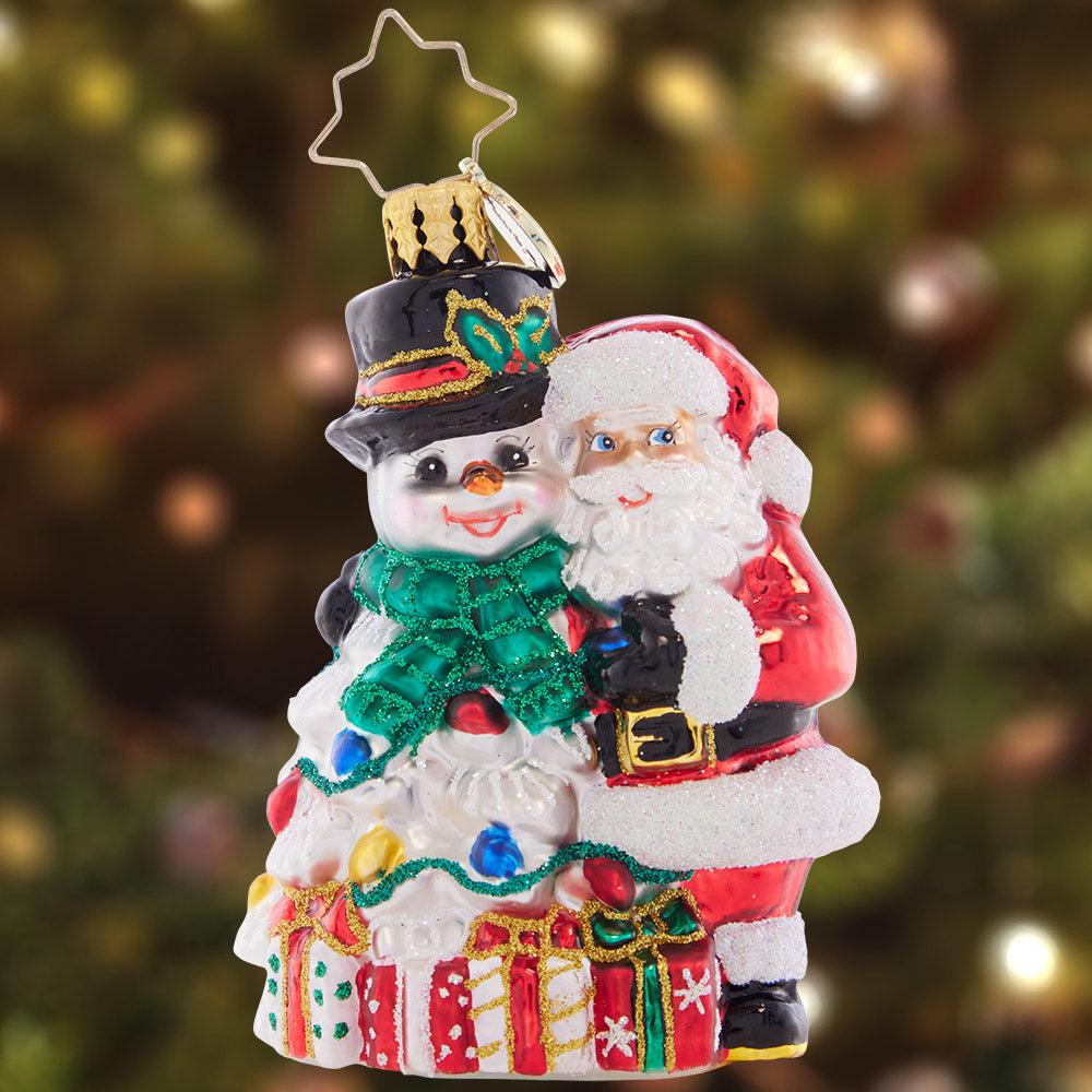 Ornament Description - A Frosty Duo Gem: The smiling Santa and Snowman are a perfect holiday pair, surrounded by beautifully-wrapped gifts and Christmas lights. 'Tis the season for festive friendship!
