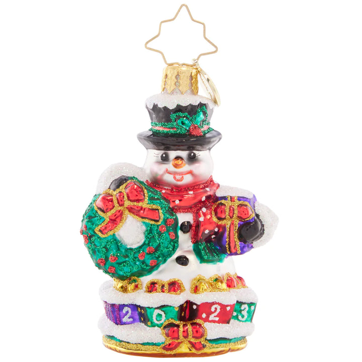 Front - Ornament Description - Holly Jolly Snowman 2023 Gem: This jolly snowman is joyfully looking ahead to the new year. Bearing a Christmas wreath and a gilded gift, he's bringing good tidings all holiday season long.