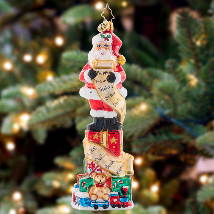 Ornament Description - Stacked Up Santa: Quite a lengthy wish list this child sent in! Much time and consideration was spent filling it in. Santa has to stand on many presents stacked to check off each gift as they're carefully packed.
