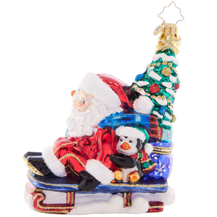 Side View 1 of 2 - Ornament Description - Christmas Getaway: Perfectly prepared with a trimmed tree, a sack of presents, and his trusty penguin pal, Santa zooms by in his speedy sled. He's got everything he needs for a cheer-filled Christmas!