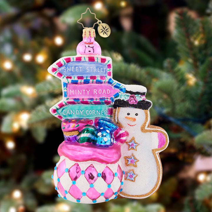 Ornament Description - Sweet Signs: Which way points to Candy Cane Lane? A jolly cookie-snowman is poised and ready to help near this bountiful gift bag-turned-directory. You'll never lose your way on Christmas Day!