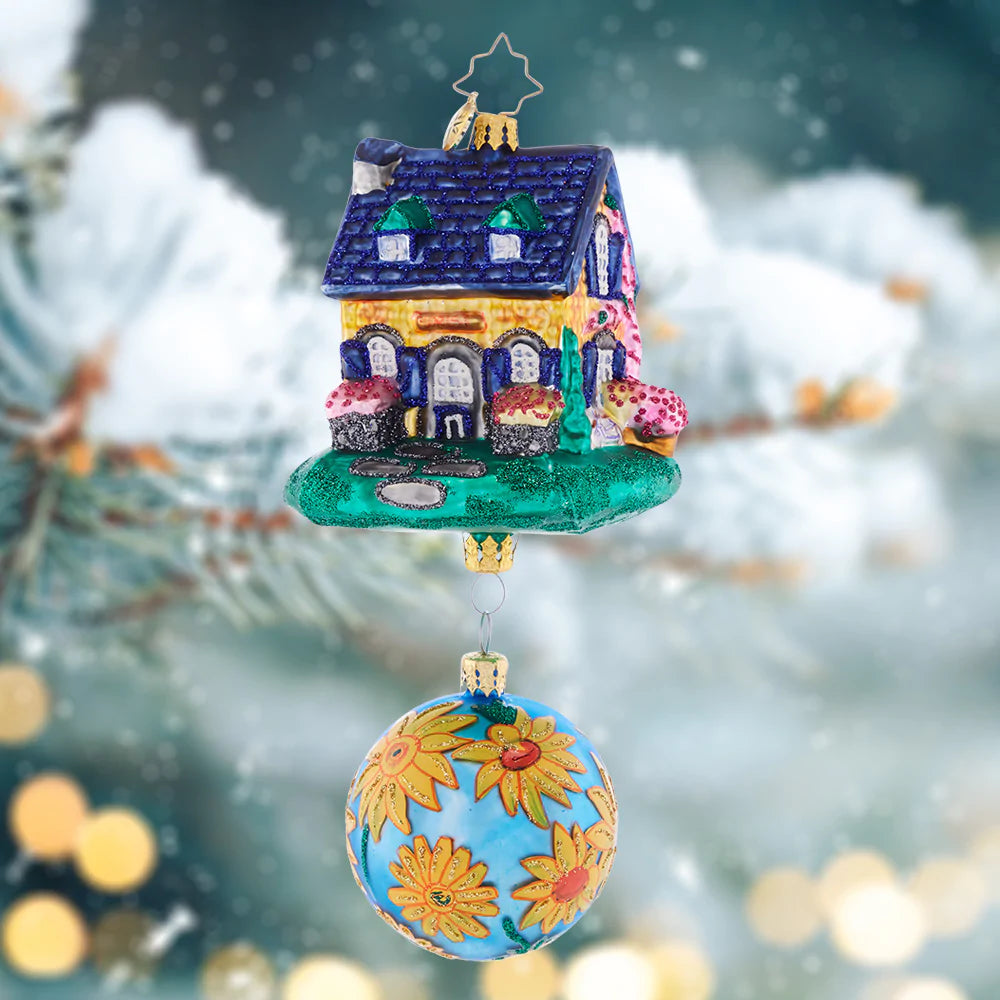Ornament Description - Countryside Cottage: A vibrant flower-adorned blue round accompanies this colorful and happy-looking house. Welcome home holiday memories with this joyful piece!