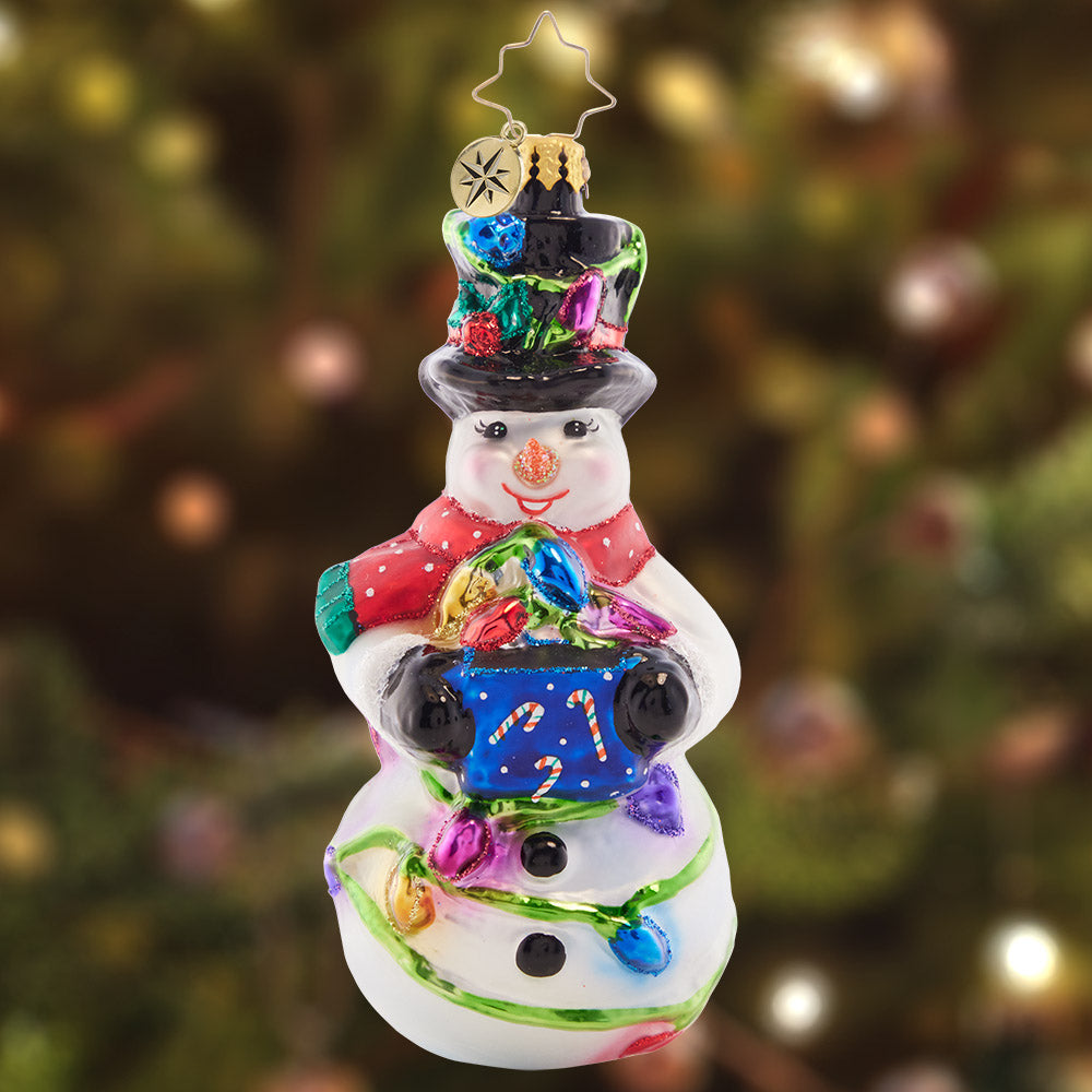 Ornament Description - Light The Night Snowman: This smiling snowman has his work cut out for him with a big bundle of holiday lights – ready to deck the halls and shine bright through the night!
