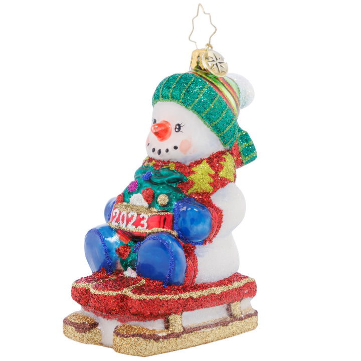 Front - Ornament Description - Sliding Through the Year: This little snowman is riding his toboggan sled into the Christmas season, looking forward to more winter fun before the holidays are all done!