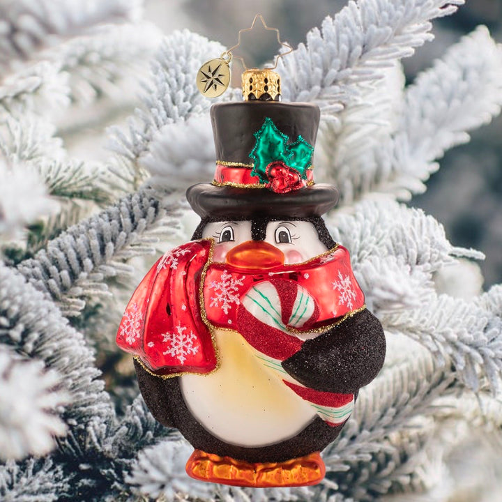 Ornament Description - Flightless Yet Fashionable: He may not be able to fly, but this bird sure has style! Mr. Penguin waddles into our hearts in his festive scarf and top hat, snacking on his favorite tasty treat!