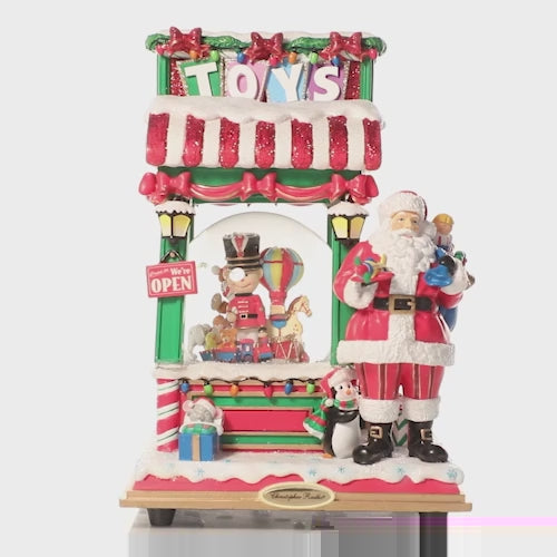 Video - Snowglobe Description - Toy Shop Santa Snowglobe: Come one, come all, to the grand opening of Santa's Toy Shop! This charming snowglobe showcases a plethora of playthings, highlighting Santa's talented toy-making skills. He's ready to bring holiday cheer to all of the good little girls and boys this year, giving a greeting and a grin at the snowy storefront. This video shows the snowglobe spinning slowly. 
